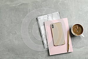 Cup of coffee with copybooks, phone and pen on grey background