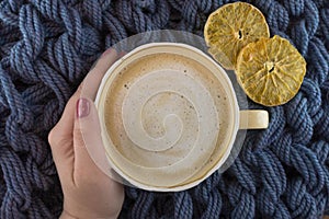 A Cup of coffee in a cozy style on a blue knitted blanket background. Slices of dried orange