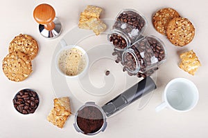 Cup of coffee, crackers, cookies, holder with ground coffee, tamper and cans of coffee beans on table. View from above