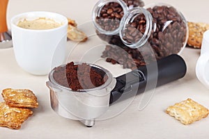 Cup of coffee, crackers, holder with ground coffee and cans of coffee beans on table