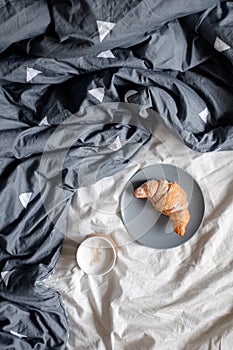A cup of coffee and a croissant on a plate on a cozy bed