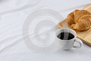 A cup of coffee and croissant on white bed