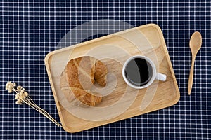 A cup of coffee and croissant with white flower