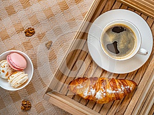 Cup of coffee and croissant in wooden box and bowl with colored cakes