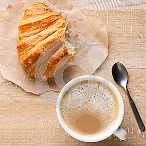 Cup of coffee and croissant on wooden table