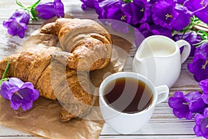 Cup of coffee, croissants, milk jar and lilac flowers