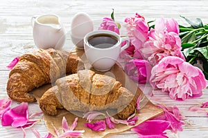 Cup of coffee, croissants, milk jar and peonies flowers