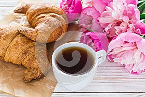 Cup of coffee, croissants, milk jar and peonies flowers