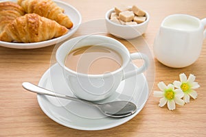 Cup of coffee, croissants, milk jug and sugar on table