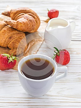 Cup of coffee, croissants, strawberry and milk jar