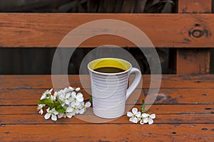 A cup of coffee on a dark, worn rustic wooden table. The composition is decorated with a twig with white flowers. Cherry tree