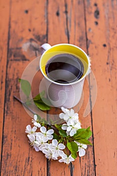 A cup of coffee on a dark, worn rustic wooden table. The composition is decorated with a twig with white flowers. Cherry tree