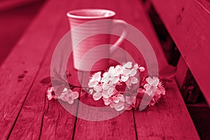 A cup of coffee on a dark, worn rustic wooden table. The composition is decorated with a twig with white flowers. Cherry tree