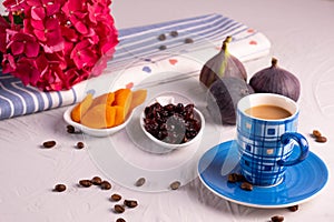 A cup of coffee, dried apricots and cranberries, fresh figs, a hydrangea branch and sprinkled coffee beans