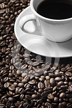 Cup of coffee drink sitting on a bed of roasted coffee beans background.