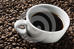 Cup of coffee drink sitting on a bed of roasted coffee beans background.