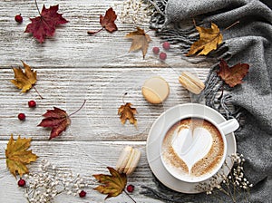 Cup of coffee and dry leaves on white wooden background