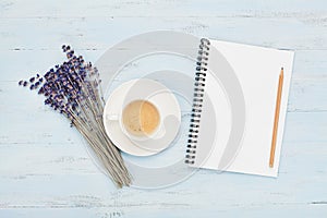 Cup of coffee, empty notebook and lavender flower on blue table top view. Woman working desk. Cozy breakfast. Flat lay style.