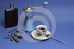 Cup of coffee, flask with cognac and manual coffee grinder on a blue background