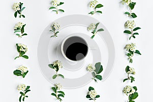 Cup of coffee and flowering Spirea arguta brides plant branches on white table. Flat lay, top view