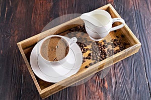 A Cup of coffee with foam and coffee beans in a wooden box on a dark wooden background,top view