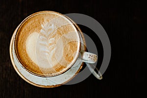 a cup of coffee with a foam pattern on a dark wooden background top view