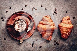 Cup of coffee and fresh croissants on a dark brown rustic background. Top view, flat lay