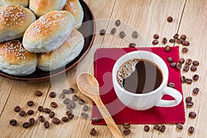 Cup of coffee and fresh fragrant buns with sesame seeds on a wooden table