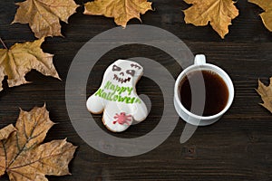 Cup of coffee and funny Halloween cookies with words Happy Halloween. Autumn background with yellow leaves. Top view