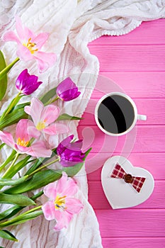 Cup of coffee, gift box in form of heart and tender bouquet of beautiful tulips on pink wooden background