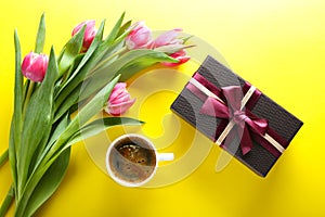Cup of coffee, gift box and pink tulips on yellow background, to