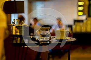 Cup of coffee, glass teapot of hot water, cafe in the morning. Image with blur in low key, for background use. Concept