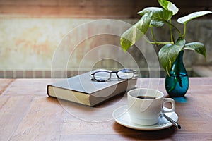 Cup of coffee and glasses on top of readbook on wood table.