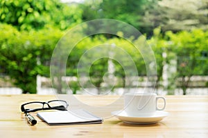 Cup of coffee with glassess and notepad on wooden table over gre