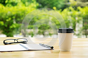 Cup of coffee with glassess and notepad on wooden table over gre