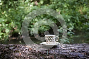 A cup of coffee with golden patterns, in a small saucer, stands on a log