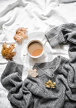 Cup of coffee, gray warm knitted sweater oversize, yellow dry leaves on the bed - cozy home still life
