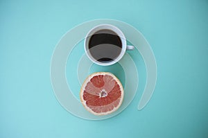 A cup of coffee on and a half of grapefruit on blue.