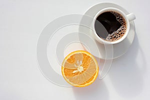 Cup of coffee and half of orange fruit on white background. Top view, copy space. Morning espresso on table. Healthy breakfast.