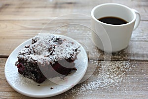 Cup of coffee with handmade chocolate cake on wooden table background. Brownie with cherries on a white plate.