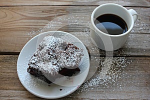 Cup of coffee with handmade chocolate cake on wooden table background. Brownie with cherries on a white plate.