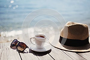 Cup of coffee, hat and sunglasses on table with beautiful sea view at background. Travel, vacations, summer fun, tourism concept