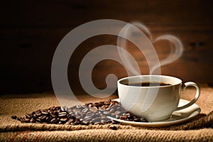 Cup of coffee with heart shape smoke and coffee beans on burlap sack on old wooden background