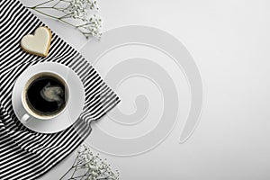 Cup of coffee, heart shaped cookie, napkin and flowers on white background, top view