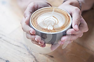 A cup of coffee hold on womenâ€™s hands that have top by foamed
