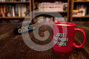 Cup of coffee with inscription Just one more episode and tv remote controller