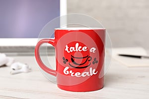 Cup of coffee with inscription Take a Break on white wooden table in office