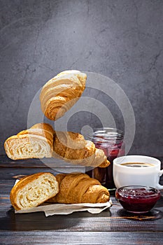 Cup of coffee, jam and flying croissants on a dark background. French breakfast