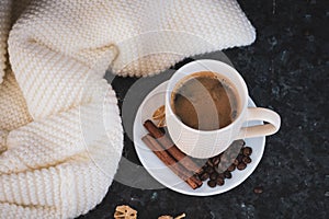 A cup of coffee is the key to a good mood. On a black, dark textural background, a composition of white, cream scarf and a white