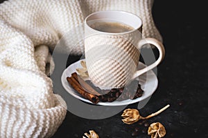 A cup of coffee is the key to a good mood. On a black, dark textural background, a composition of white, cream scarf and a white